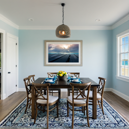 An Art Wall Room Mockup generated with AI for Print On Demand Seller. The mockup features a Coastal Style Dining Room with a framed photography print of a cloudy sunset over a Caribean Sea on the wall